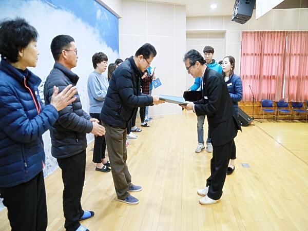  승진 및 보직변경된 직원들이 무대로 나온 자리에서 관장님이 김상구 팀장에게 임명장을 전달하고 있음.    