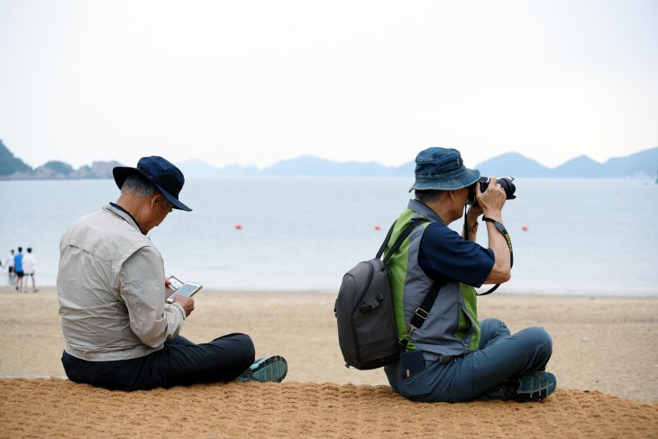  어르신 한분은 DSLR카메라로 사진을 찍고, 옆에 앉으신 어르신은 핸드폰으로 찍은 사진을 확인하고 있다   